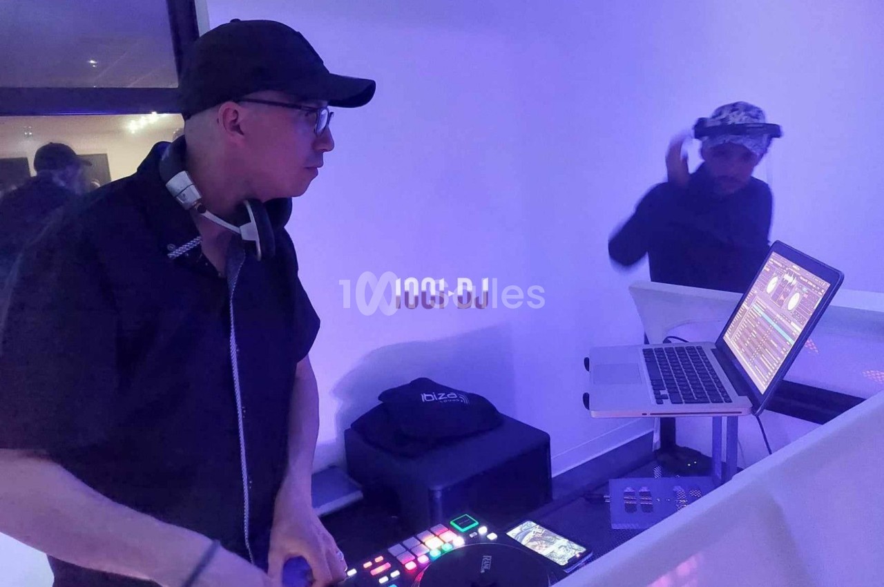 Un DJ mixe sur une table de mixage avec un ordinateur portable, dans une ambiance lumineuse violette.