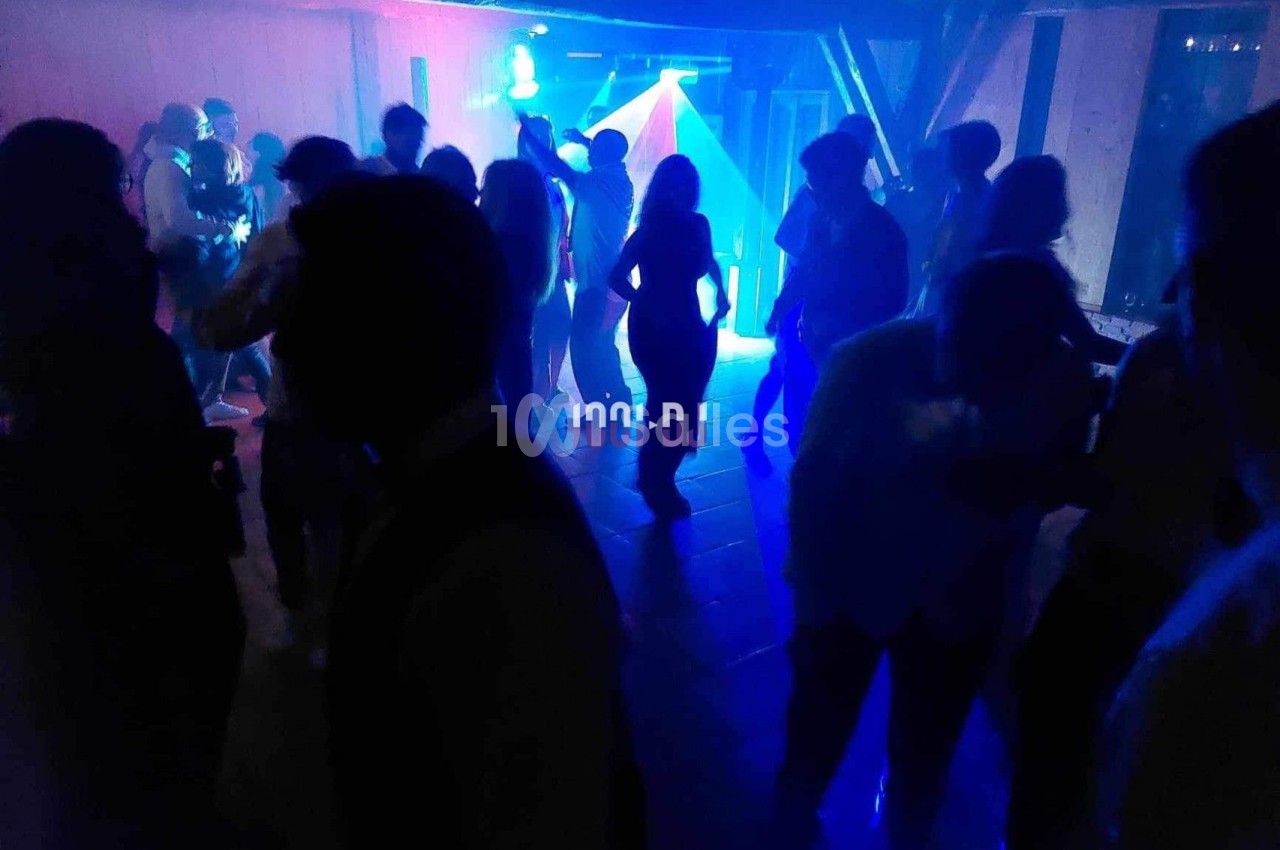 Personnes dansant dans une salle sombre éclairée par des lumières colorées et un projecteur.