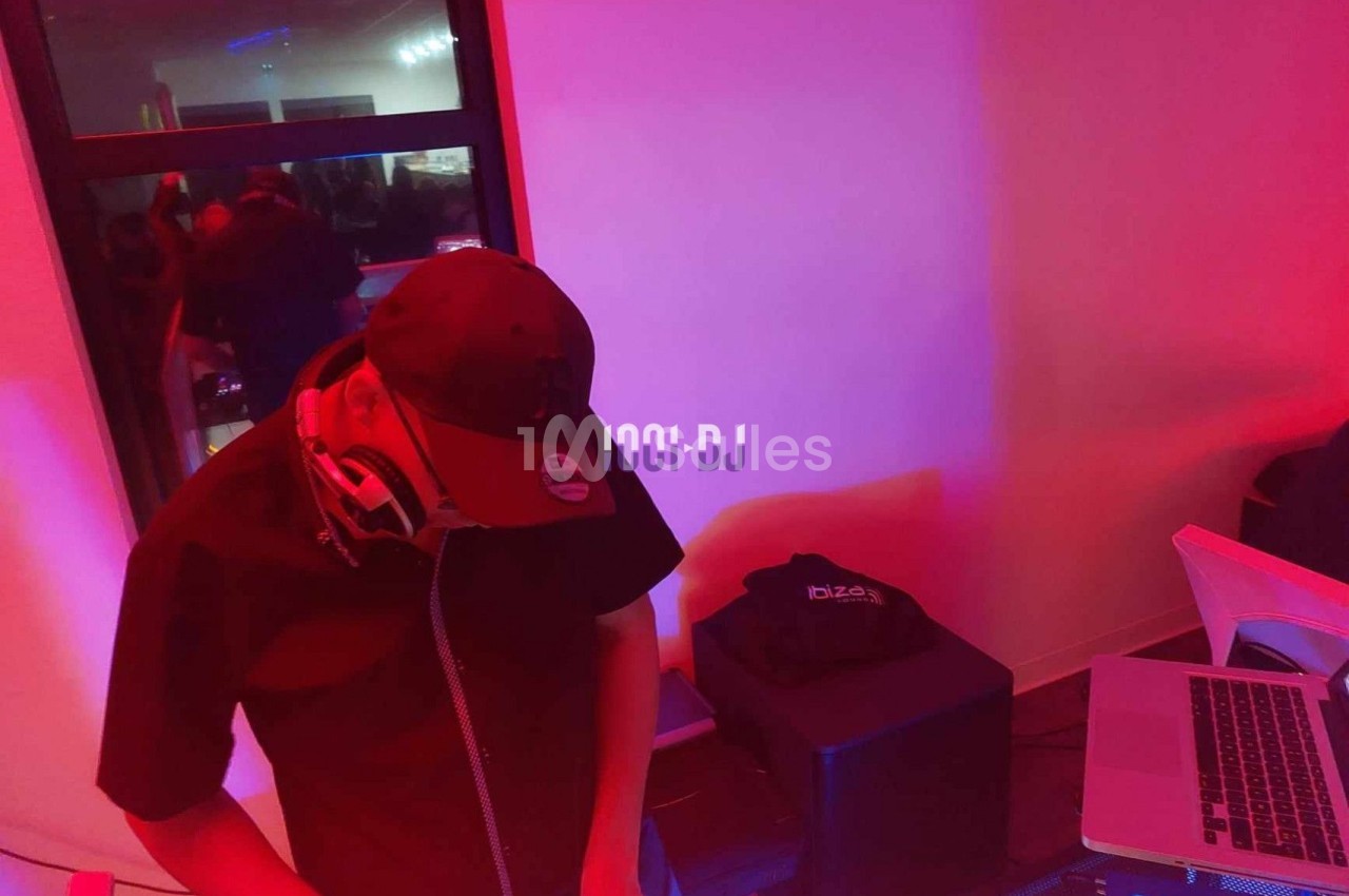 Un DJ portant une casquette mixe de la musique sur une console dans une ambiance lumineuse rouge et violette.