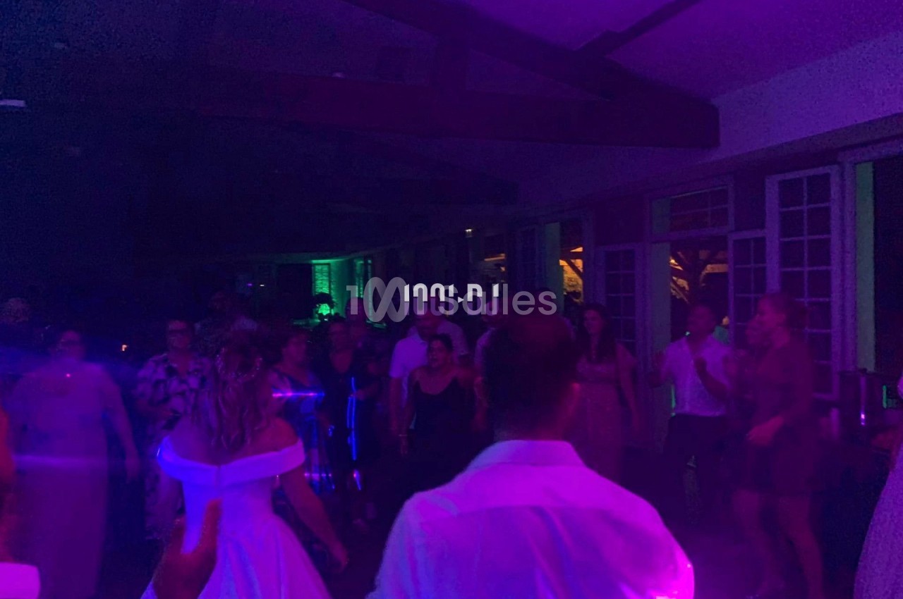 Des personnes dansent dans une salle faiblement éclairée avec des lumières colorées, lors d'une fête ou d'un événement.