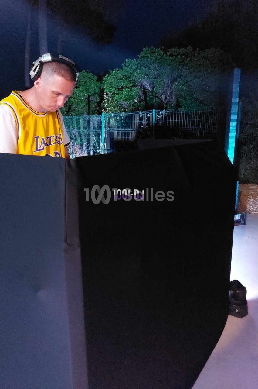 Un DJ portant un casque audio mixe de la musique en extérieur, devant un équipement éclairé dans la nuit.