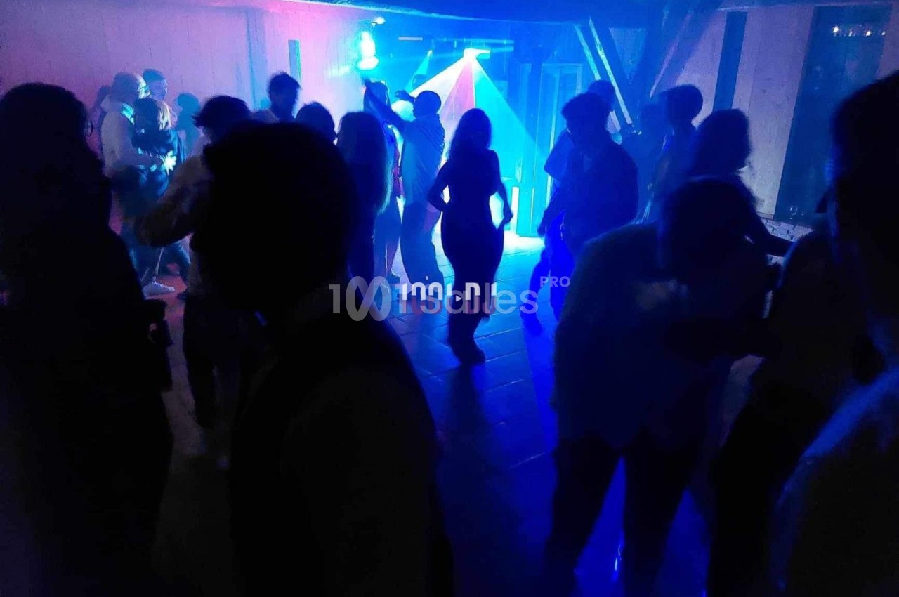Personnes dansant dans une salle sombre éclairée par des lumières colorées et un projecteur.