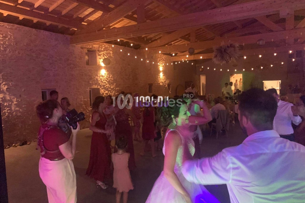 Des invités dansent lors d'une fête dans une salle en pierre éclairée par des guirlandes lumineuses.