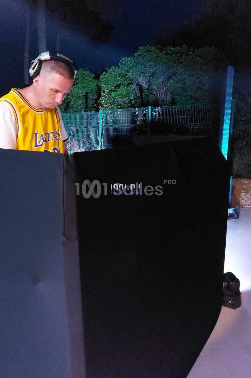 Un DJ portant un casque audio mixe de la musique en extérieur, devant un équipement éclairé dans la nuit.