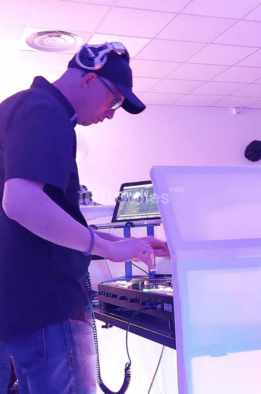 Un DJ mixant de la musique sur une table de mixage dans une salle éclairée par des lumières violettes.