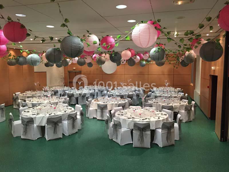 Salle de réception décorée avec des lanternes suspendues et des tables rondes dressées pour un événement.
