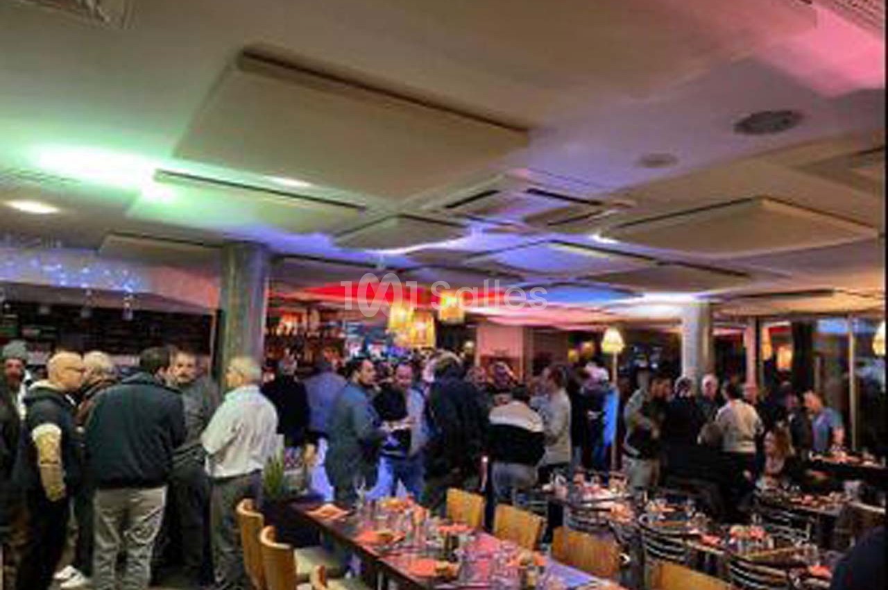 Salle de restaurant animée avec des convives debout près du bar et des tables dressées en premier plan.