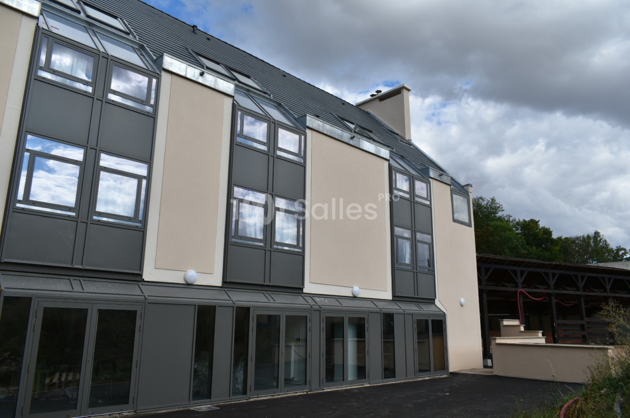 Façade d'un bâtiment moderne à plusieurs étages avec de grandes fenêtres et un toit incliné sous un ciel nuageux.