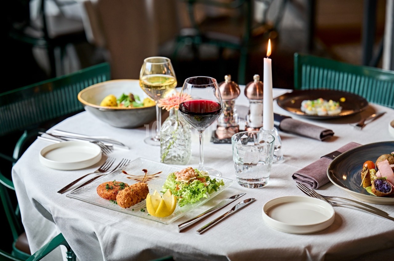 Table dressée avec des plats raffinés, verres de vin, bougie allumée et couverts sur une nappe blanche.