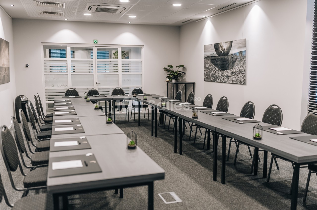 Salle de réunion moderne avec tables disposées en U, chaises, blocs-notes et décoration murale.