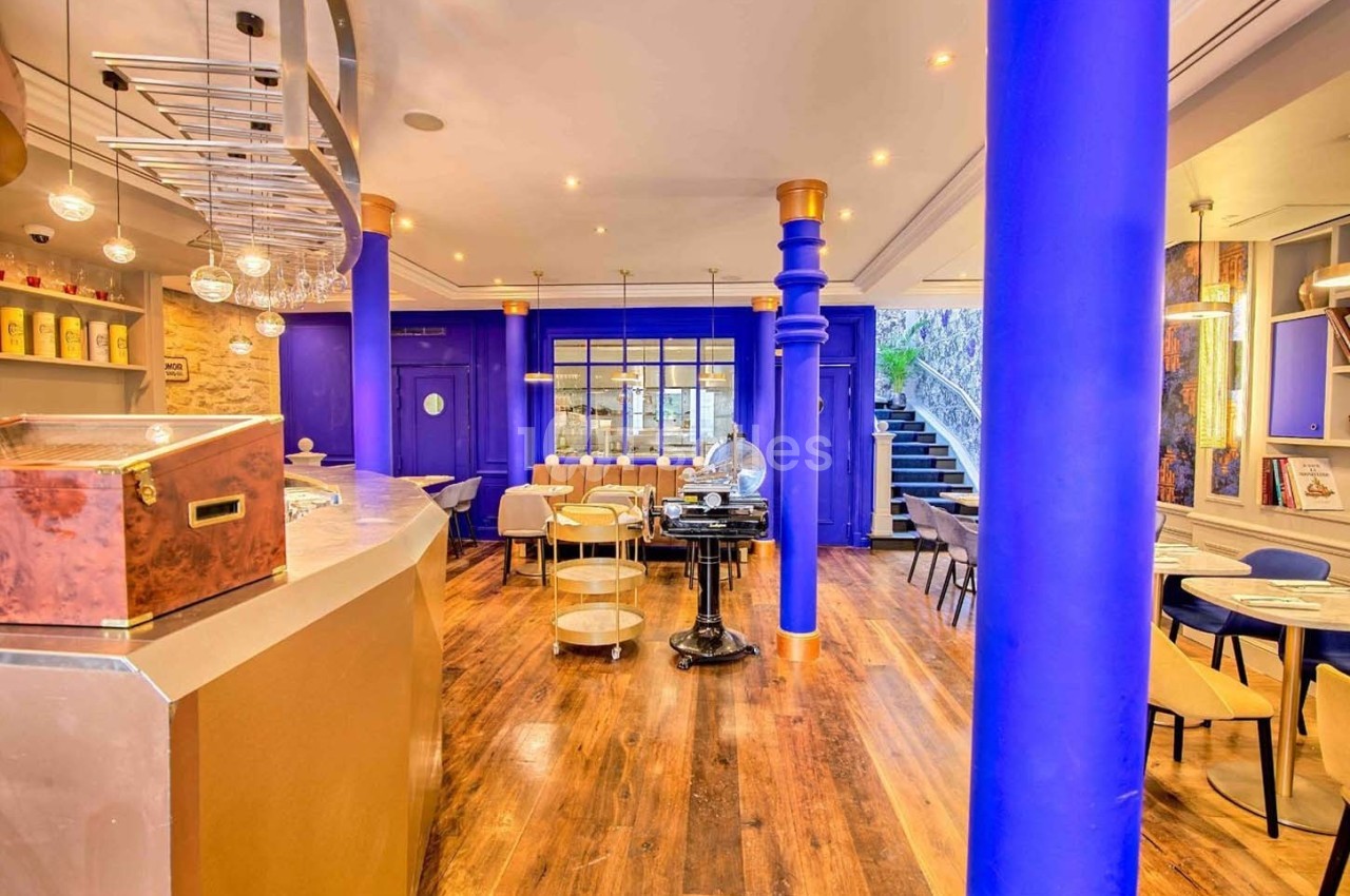 Intérieur d'un café moderne avec colonnes bleues, mobilier clair, parquet en bois et éclairage chaleureux.