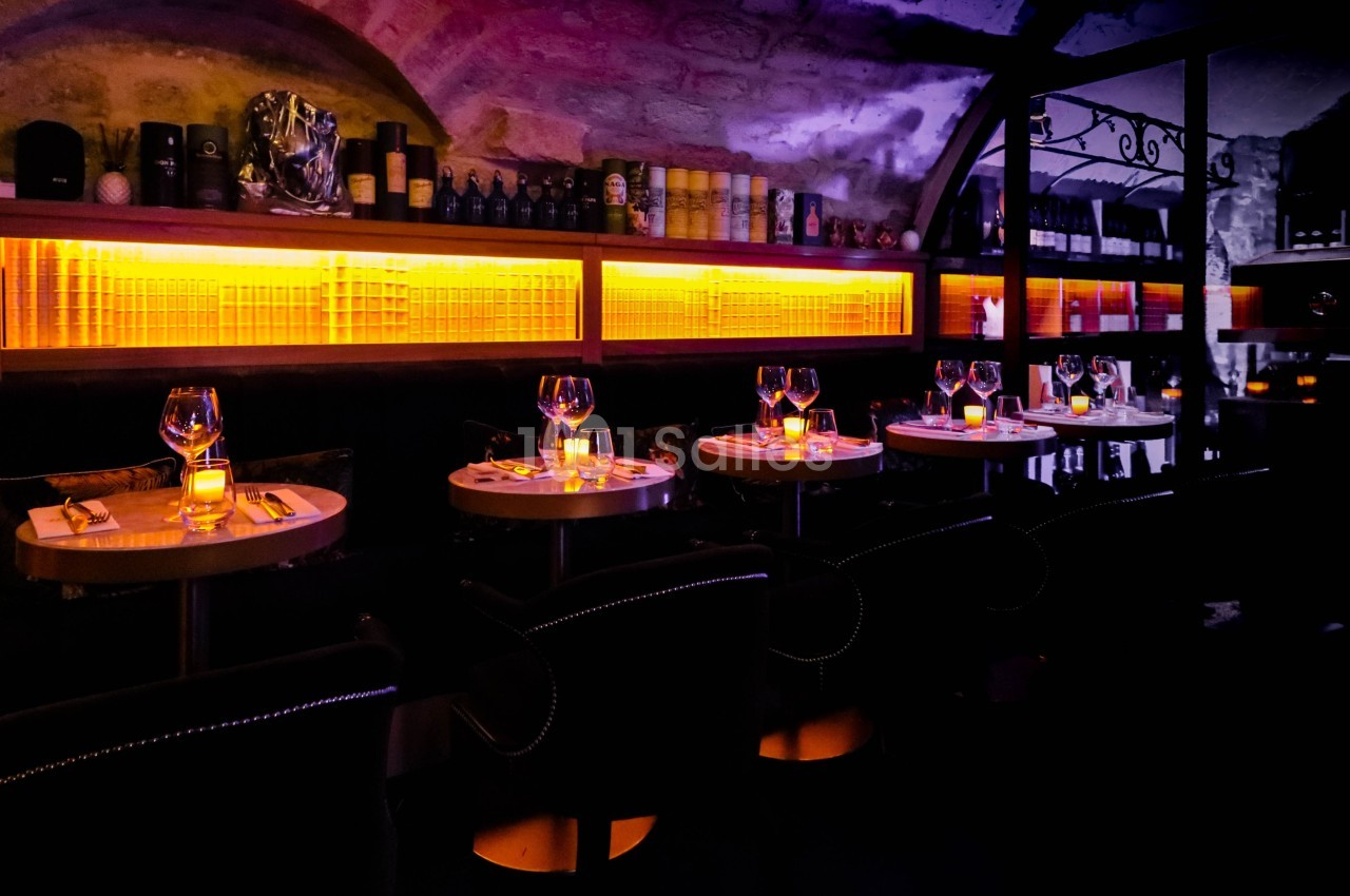 Salle de restaurant avec tables dressées, éclairage tamisé et étagères illuminées en arrière-plan.