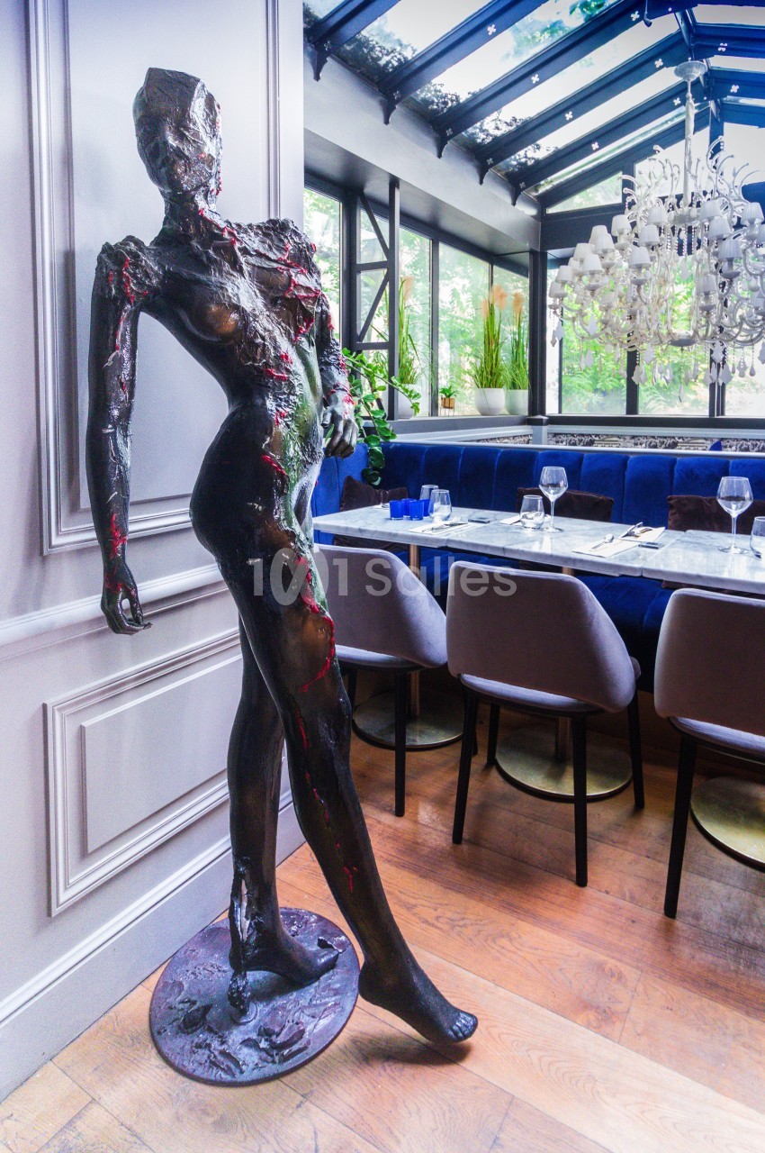 Statue moderne d'une silhouette humaine inclinée, exposée dans un restaurant lumineux avec des tables dressées.