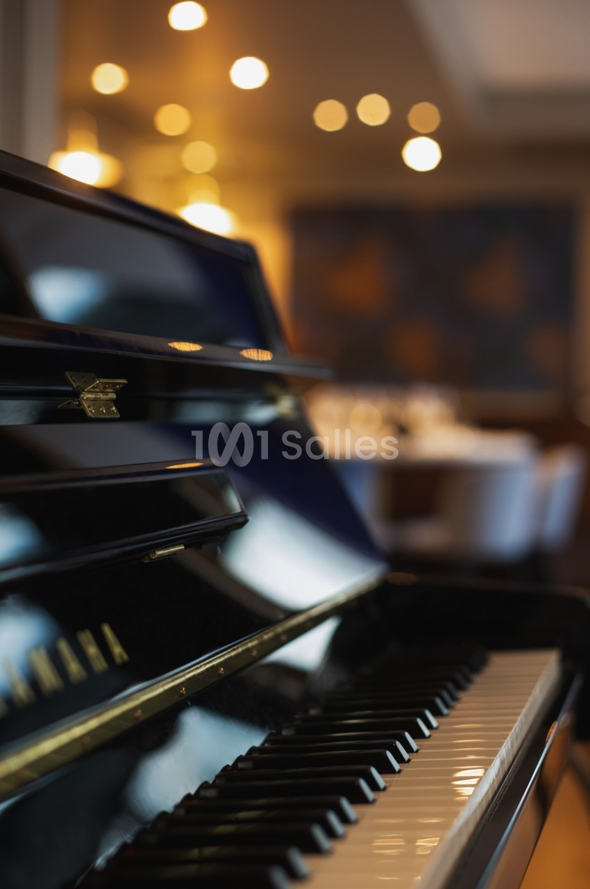 Clavier d'un piano noir brillant en gros plan, avec un arrière-plan flou d'une salle éclairée.