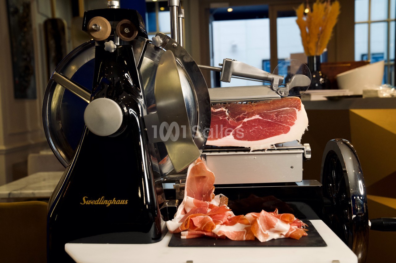 Trancheuse à jambon en métal noir avec une pièce de jambon cru et des tranches fines disposées sur une planche.