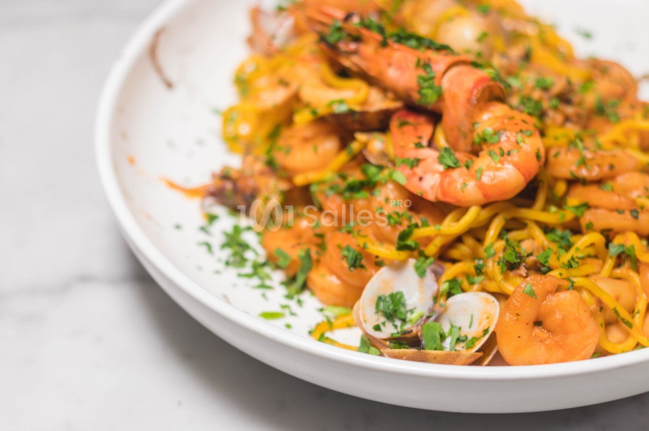 Assiette de pâtes aux fruits de mer avec crevettes, palourdes et persil, servie sur une table en marbre.