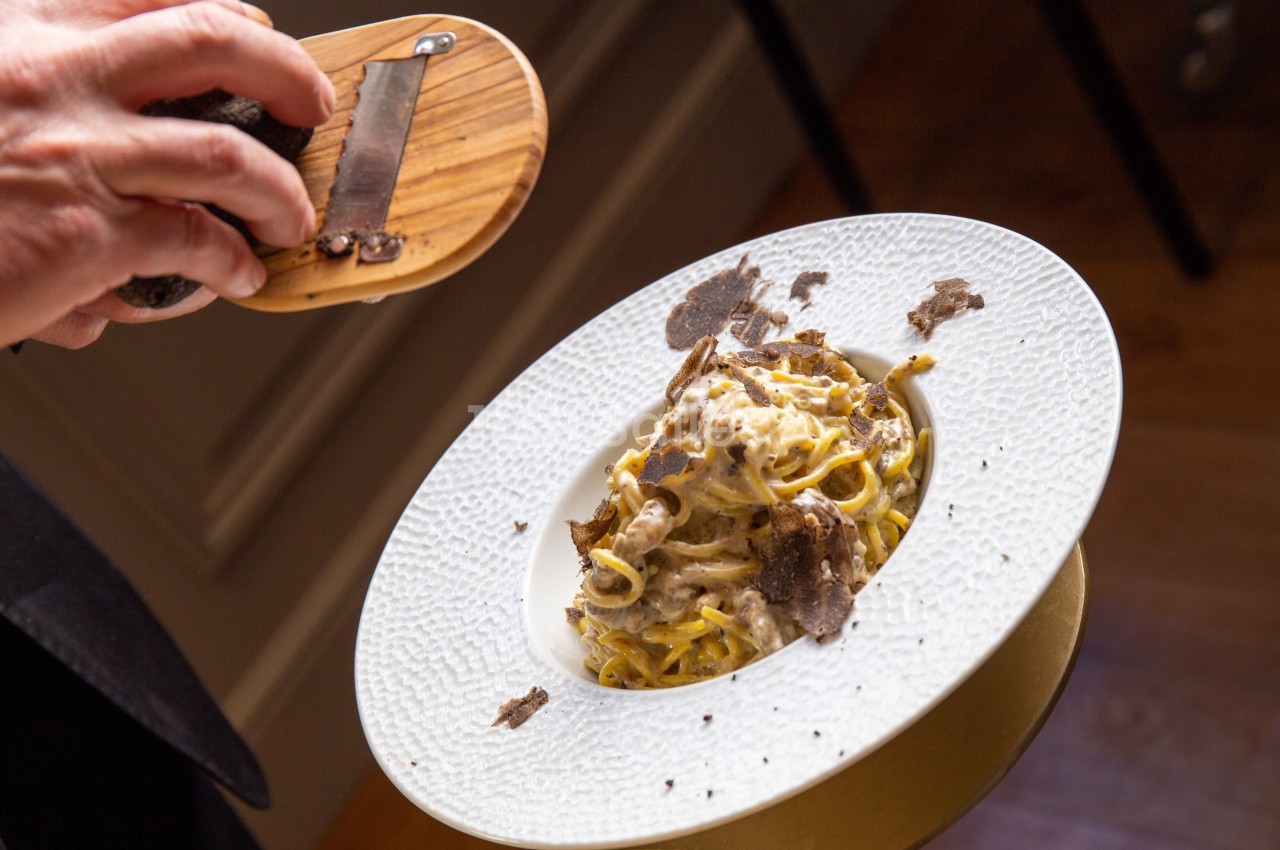 Plat de pâtes crémeuses servi dans une assiette, garni de truffes fraîches râpées à la main.