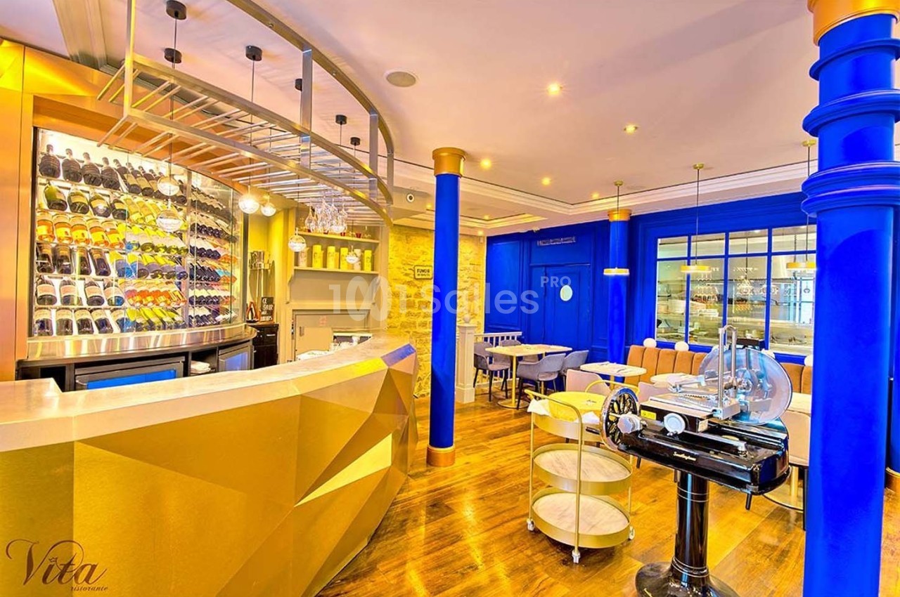 Intérieur d'un restaurant avec comptoir doré, étagères à bouteilles, murs colorés et mobilier moderne.
