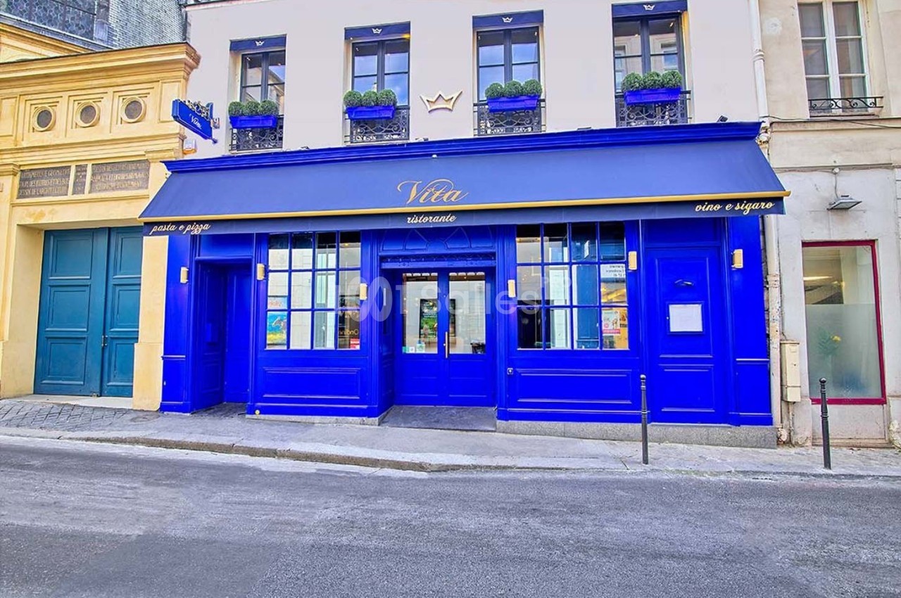 Façade d'un restaurant aux murs et volets bleus vifs, avec une enseigne et une terrasse discrète en rue calme.
