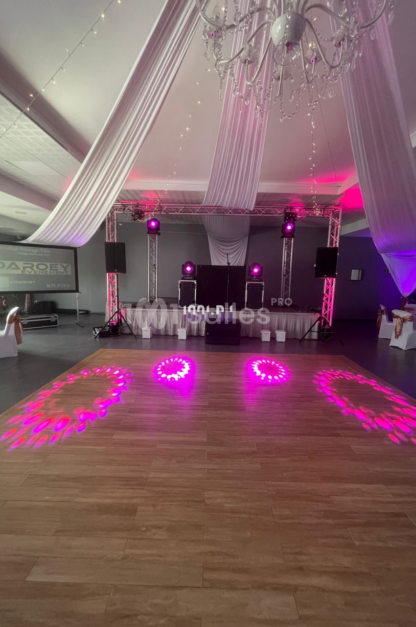 Salle de réception avec piste de danse éclairée par des lumières roses, décorée de voilages et d'un lustre suspendu.
