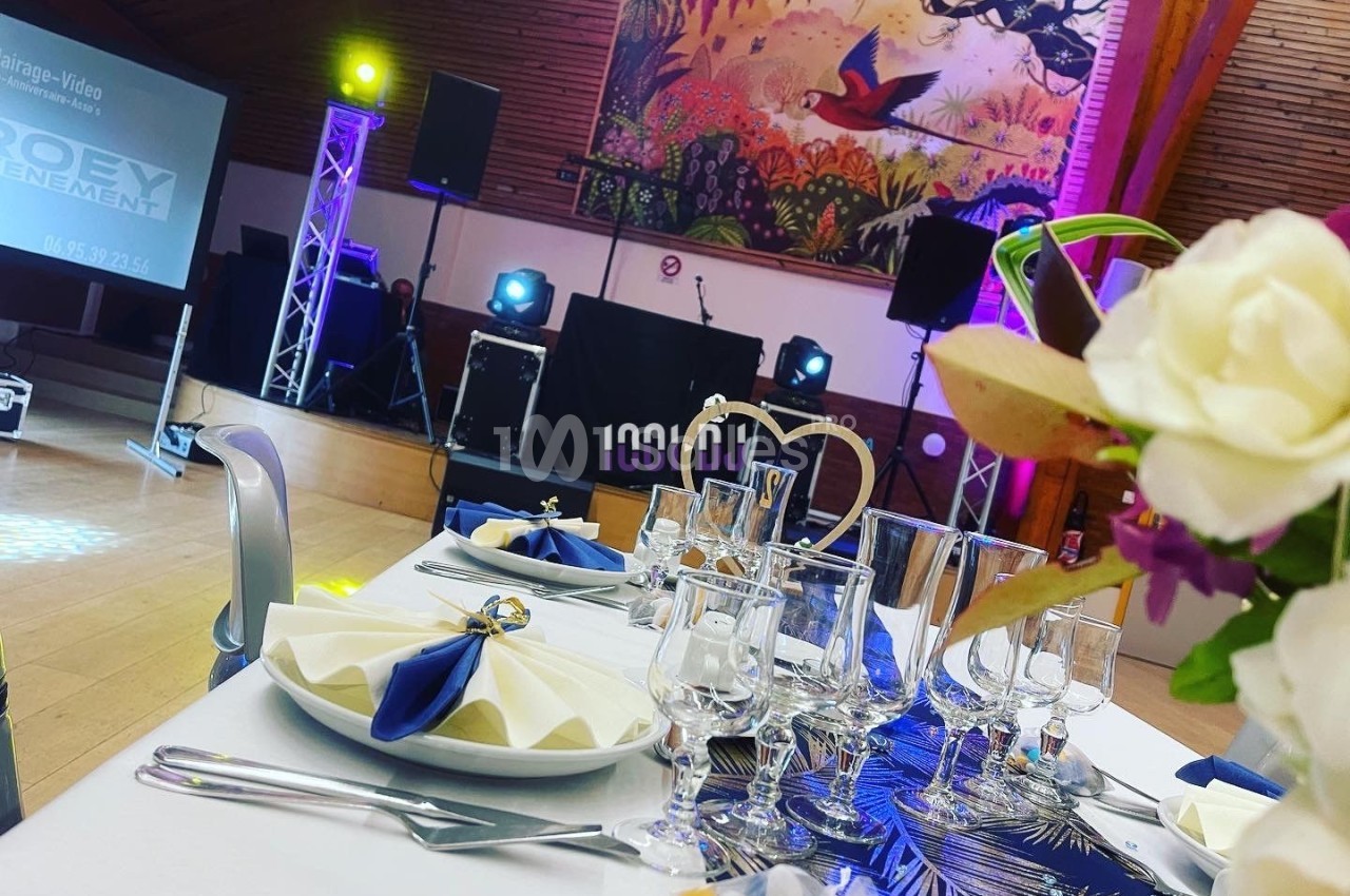 Salle de réception décorée avec une table dressée, des lumières colorées et une scène équipée pour un événement.