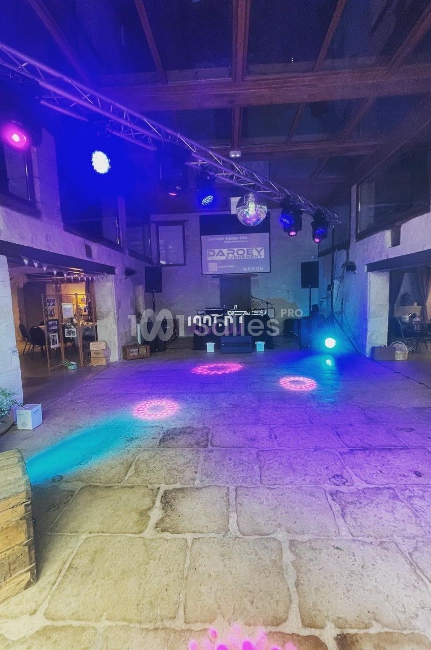Salle en pierre avec éclairage coloré, scène équipée de projecteurs et écran en fond, ambiance festive.