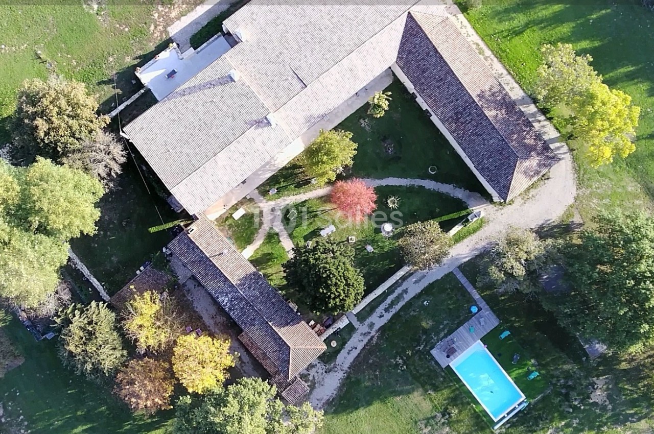Vue aérienne d'une propriété avec bâtiments en pierre, jardin arboré, allées et piscine rectangulaire.
