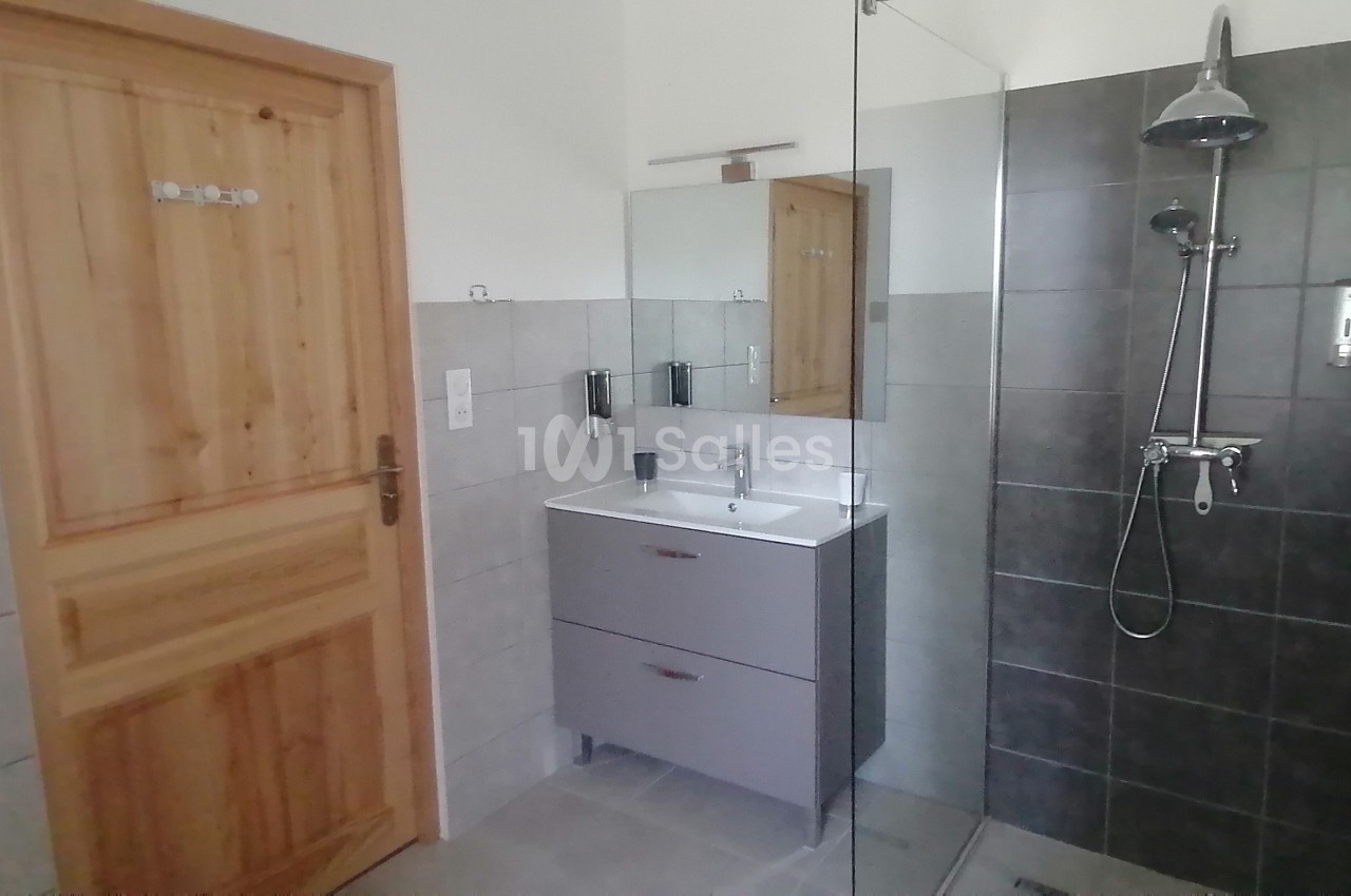 Salle de bain avec douche à l'italienne, meuble lavabo gris, miroir et porte en bois clair.