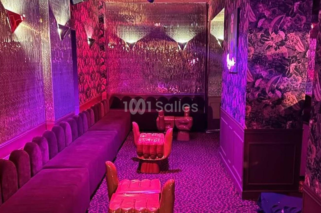Salle lounge avec banquettes rouges, fauteuils originaux et éclairage tamisé aux tons roses et violets.