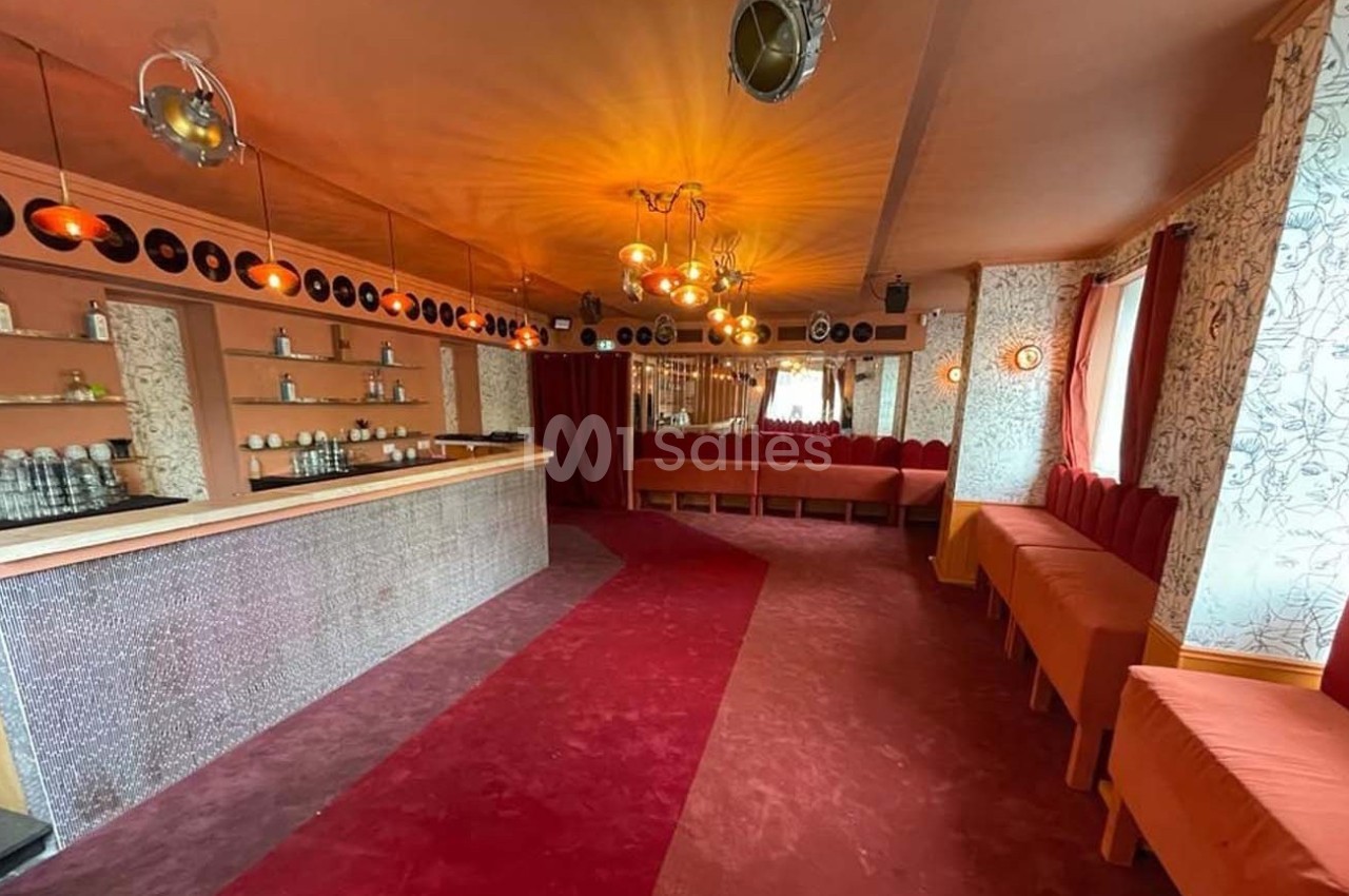 Salle avec bar, banquettes rouges, décor rétro, disques vinyles au mur et éclairage chaleureux.