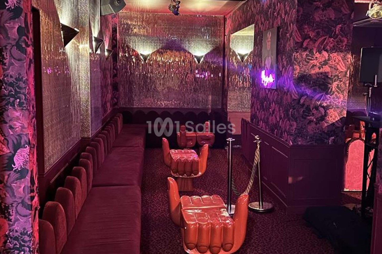 Salle décorée avec des banquettes rouges, murs fleuris et sièges en forme de mains sous un éclairage tamisé.