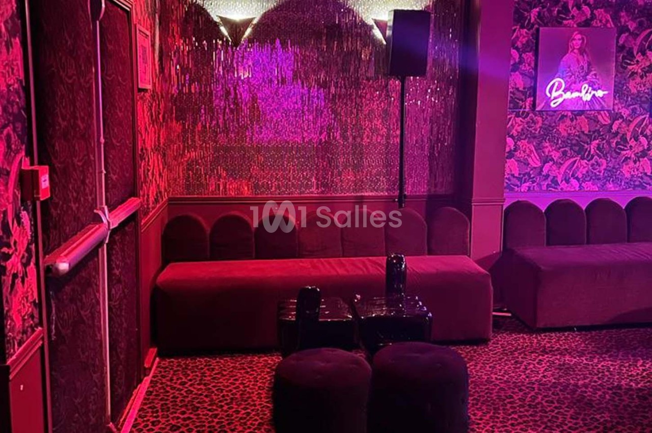 Salle décorée avec des murs rouges texturés, banquettes, tabourets noirs et éclairage tamisé rose.