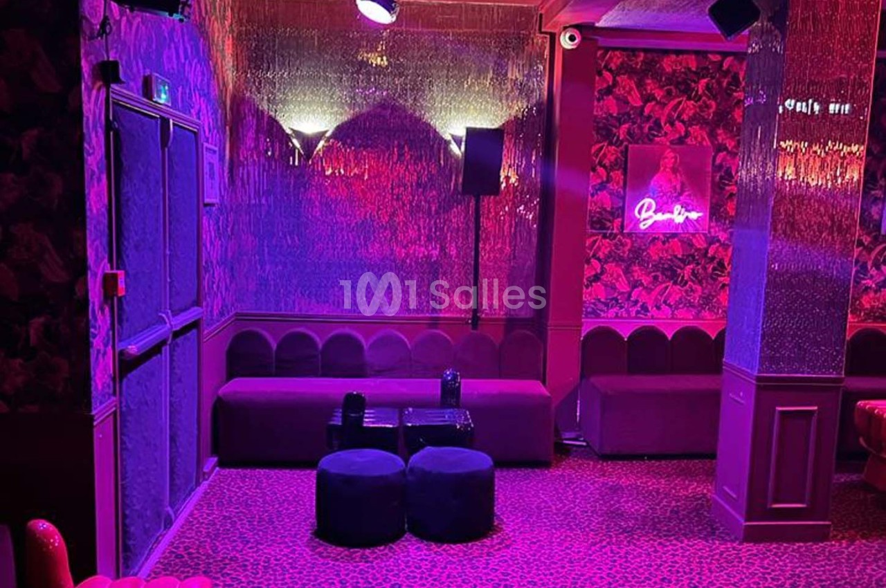 Salle aux tons roses et violets avec banquettes, poufs, murs décorés et éclairage tamisé.