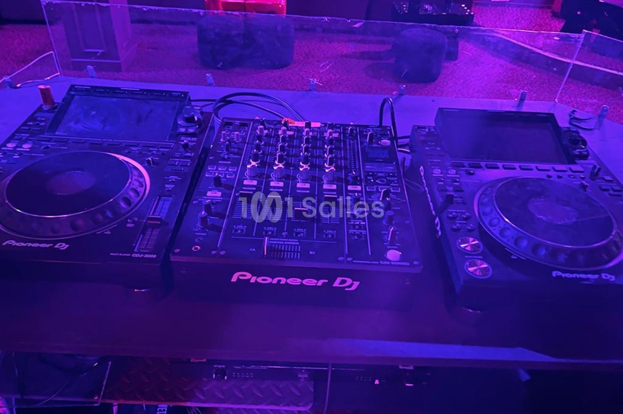 Matériel de DJ comprenant une table de mixage et deux platines Pioneer sur une table dans un environnement sombre.