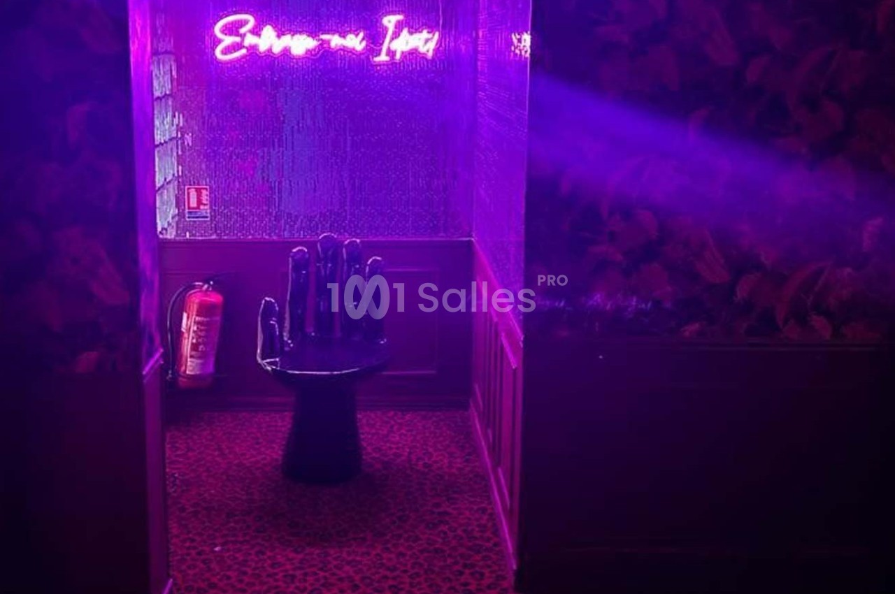 Chaise en forme de main noire dans un couloir éclairé par une lumière violette avec un néon et un extincteur au mur.