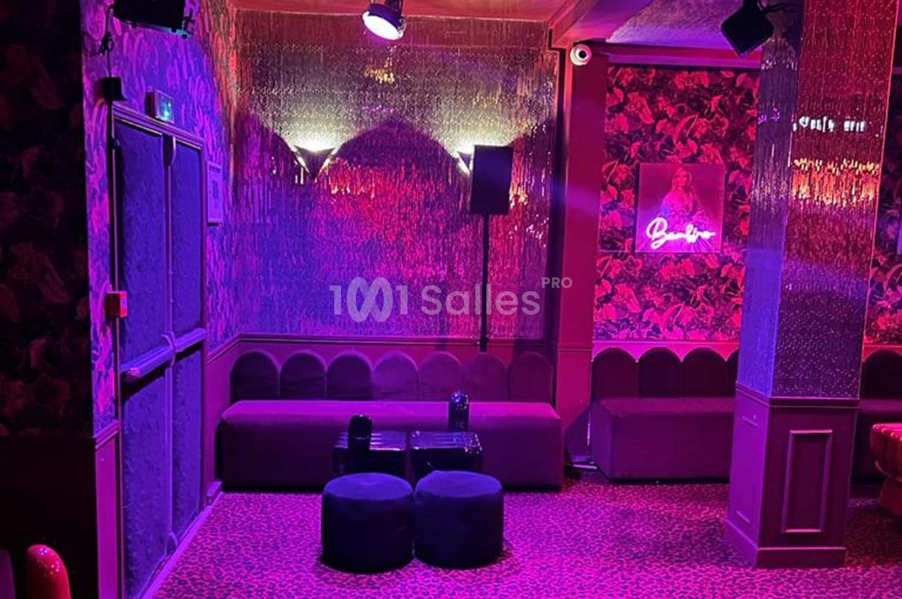 Salle de style rétro avec banquettes, tabourets et éclairage rose-violet, décorée de motifs floraux et un néon lumineux.