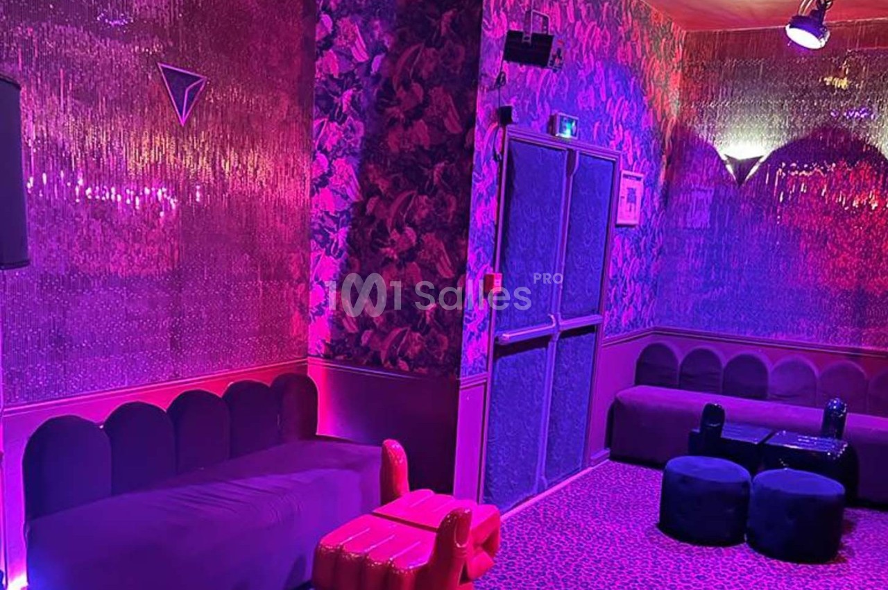 Salle décorée avec des murs texturés, éclairage rose et violet, banquettes et poufs dans un style lounge.