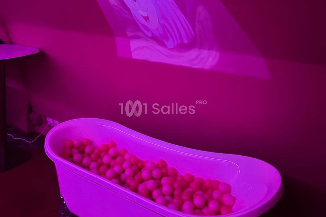 Baignoire remplie de balles roses dans une pièce éclairée par une lumière rose avec une projection murale floue.