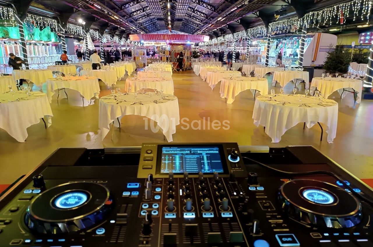 Salle de réception décorée avec des tables rondes dressées, vue depuis une console de DJ au premier plan.