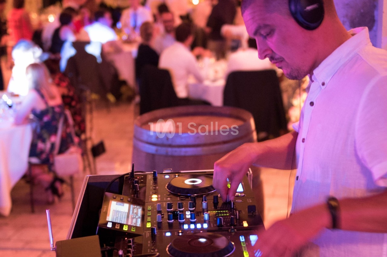 Un DJ mixe de la musique sur une table de mixage lors d'un événement avec des invités en arrière-plan.