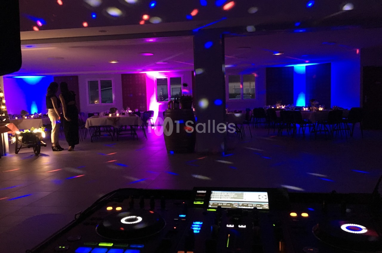 Salle de réception éclairée par des lumières colorées, avec une table de mixage au premier plan et des invités en arrière…