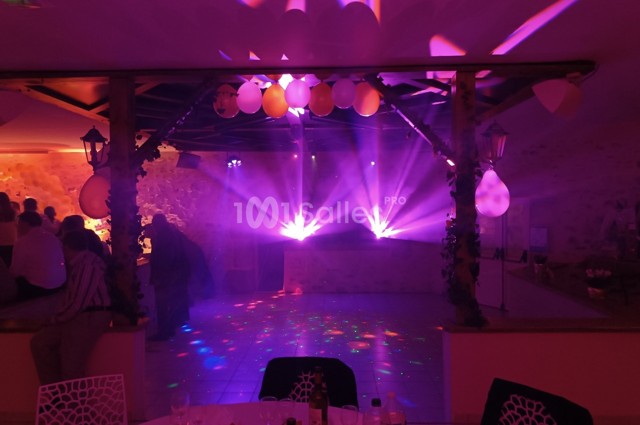 Salle de réception avec éclairage coloré, projecteurs lumineux et décorations suspendues, ambiance festive.