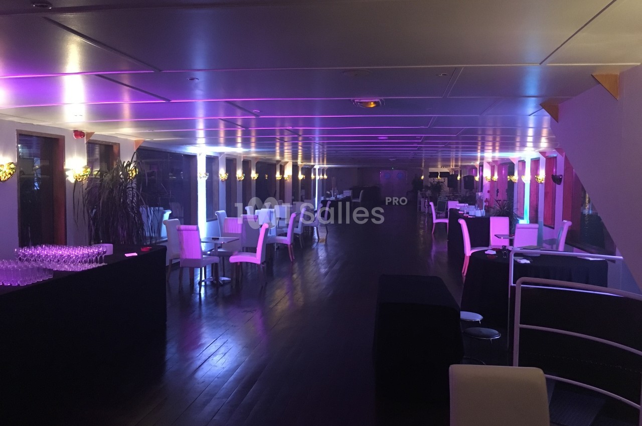 Salle de réception élégante avec tables et chaises blanches, éclairée par des lumières violettes.