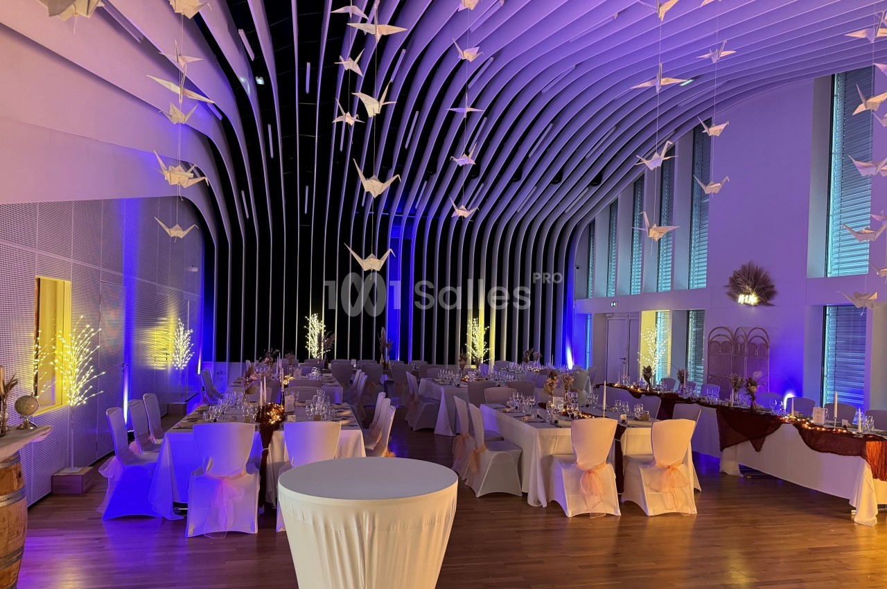Salle de réception décorée avec des tables dressées, des guirlandes lumineuses et des origamis suspendus au plafond.