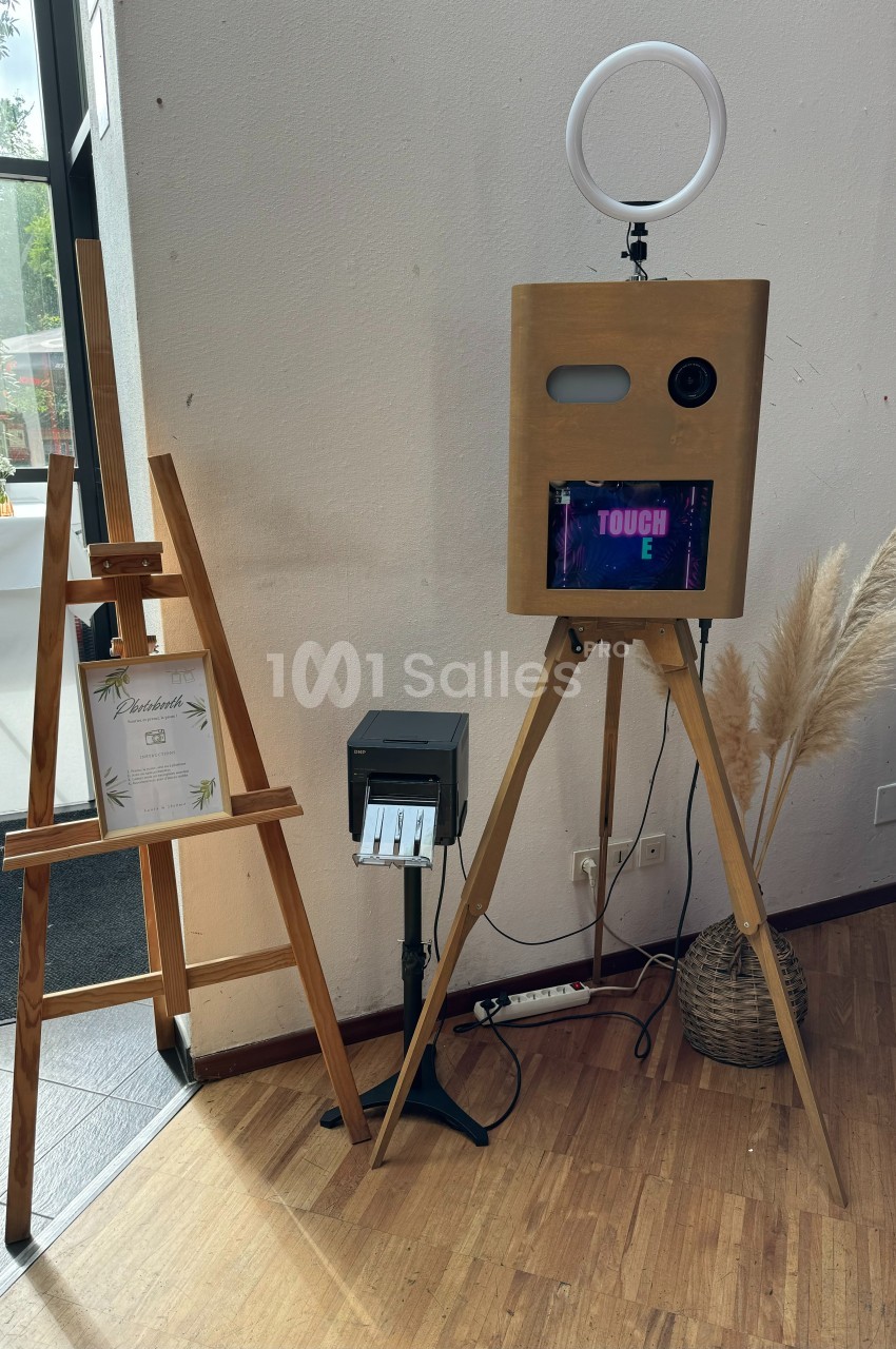 Borne photo en bois sur trépied avec écran tactile, imprimante et anneau lumineux, près d'un chevalet et d'une décoration en…