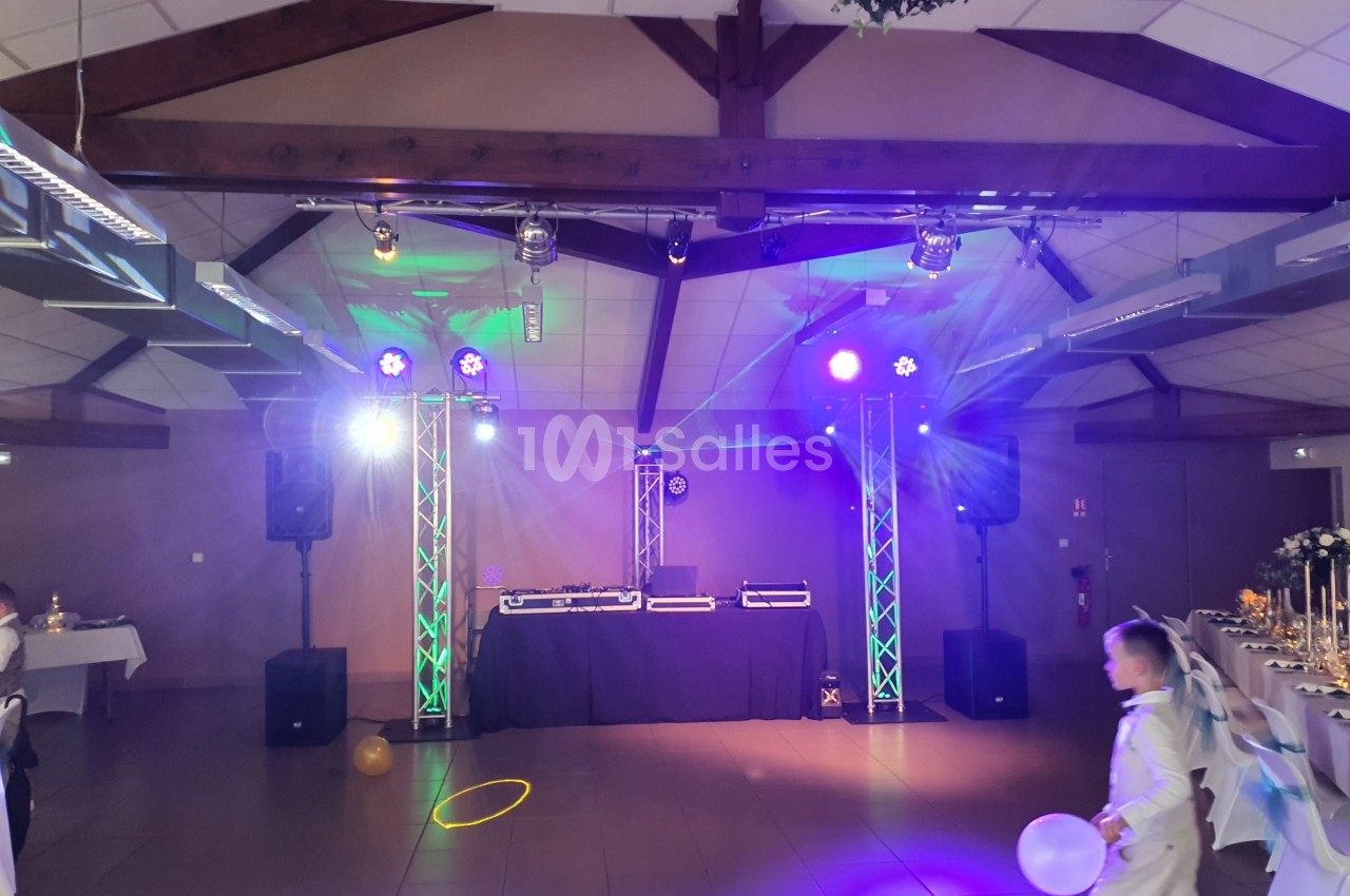 Salle de réception décorée avec éclairage coloré, piste de danse vide et matériel de DJ installé au fond.