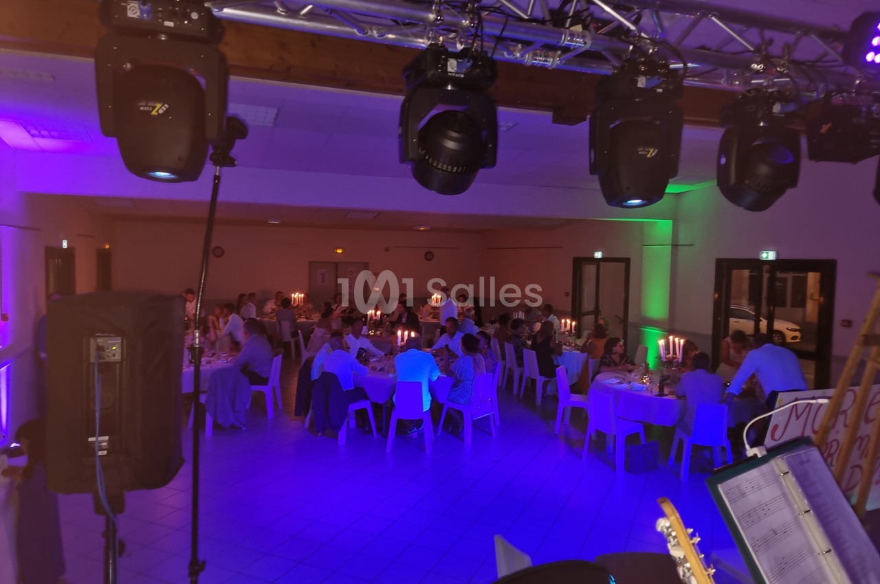 Salle de réception éclairée, avec des invités assis à des tables décorées de bougies, vue depuis une scène.