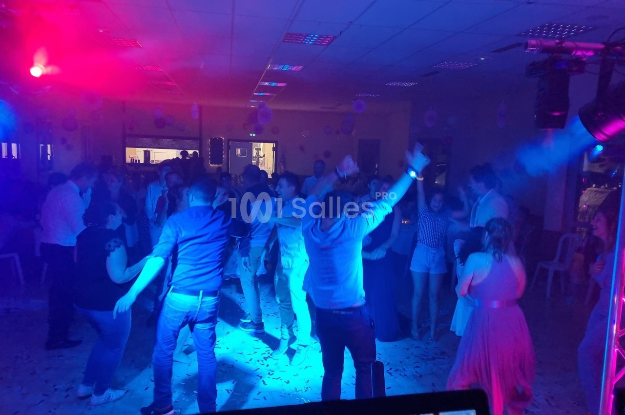 Personnes dansant sous des éclairages colorés dans une salle, ambiance festive avec musique et décorations.