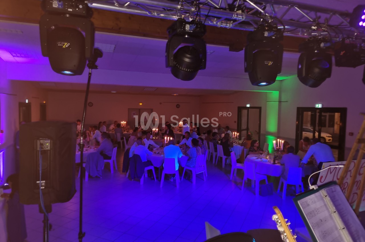Salle de réception éclairée, avec des invités assis à des tables décorées de bougies, vue depuis une scène.