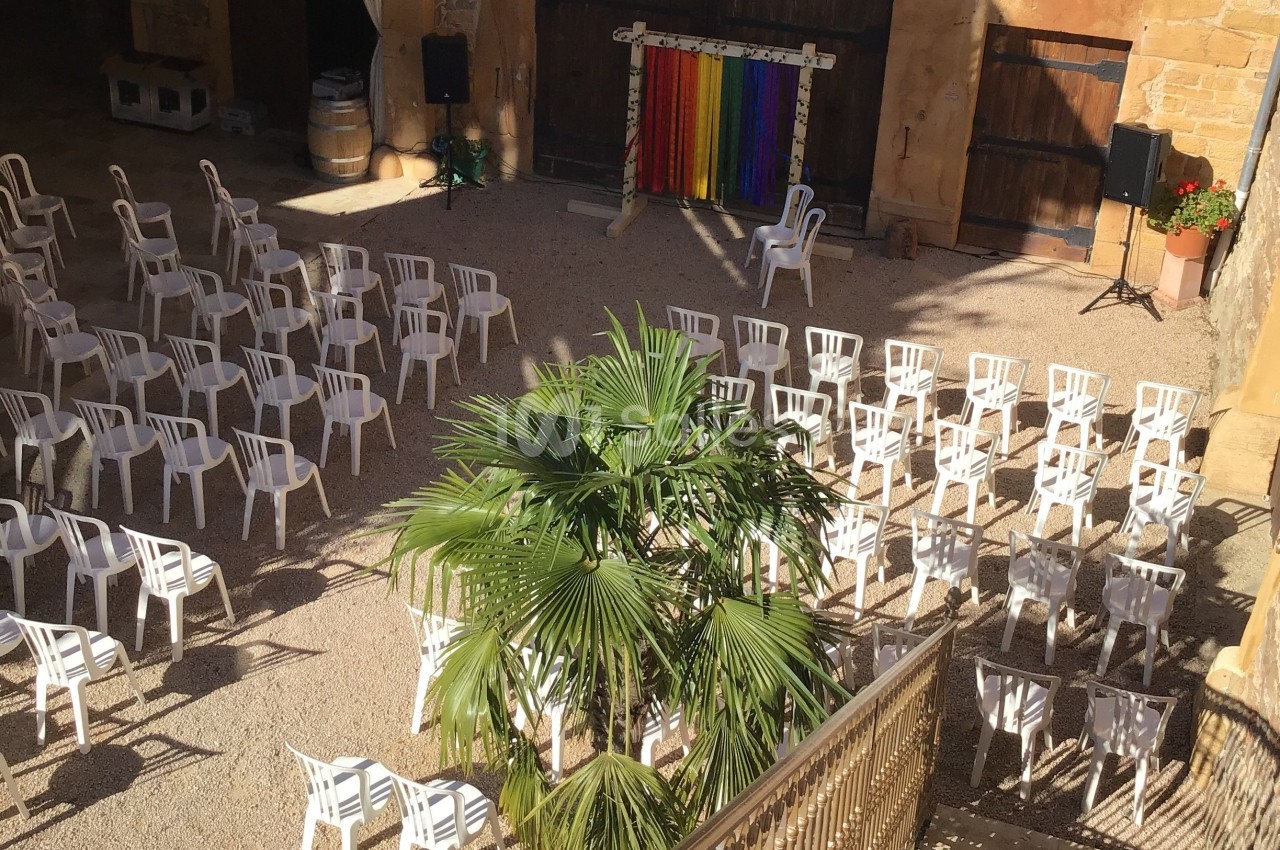Chaises blanches disposées en rangées dans une cour extérieure ensoleillée avec une scène colorée en arrière-plan.